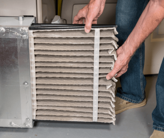 A man is holding the air filter on top of an air conditioner.